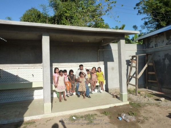 Kinder mit Pater Jaison vor den in kindgerechten Höhen angebrachten acht Waschplätzen